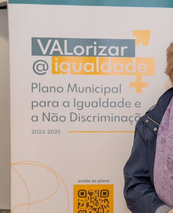 Mulher com cabelo claro segura documentos em frente a um cartaz sobre igualdade.