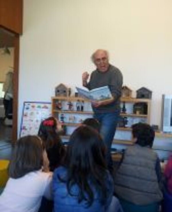 Um contador de histórias lê um livro para crianças sentadas em frente.