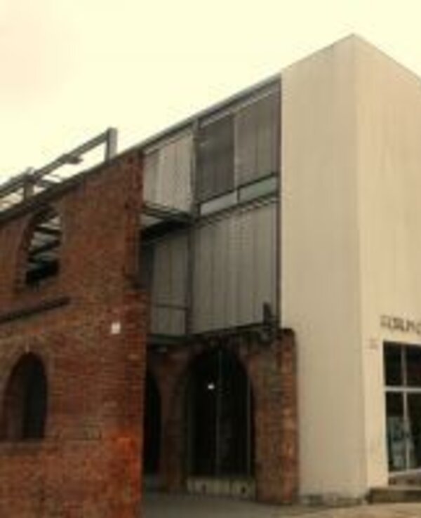 Edifício moderno com estrutura de metal e tijolos expostos, entrada ampla.