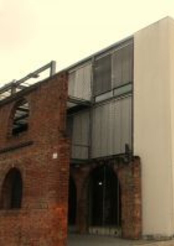 Edifício moderno com estrutura de metal e tijolos expostos, entrada ampla.