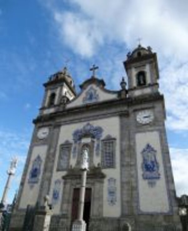 Igreja com azulejos azuis, torres e uma estátua em frente, sob céu azul.