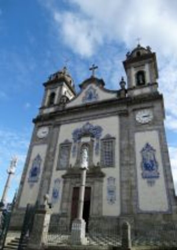 Igreja com azulejos azuis, torres e uma estátua em frente, sob céu azul.