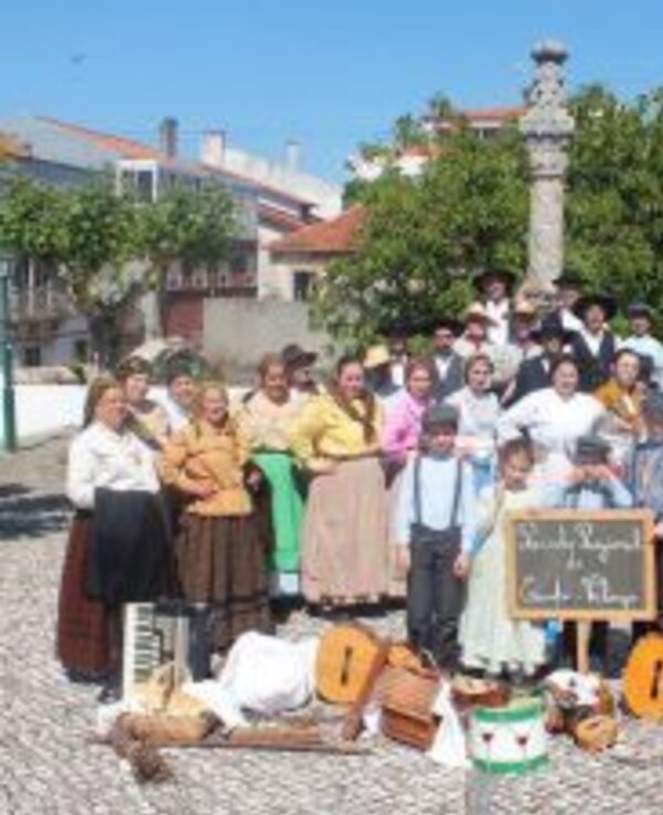 Grupo de pessoas em trajes tradicionais, com instrumentos e uma placa.