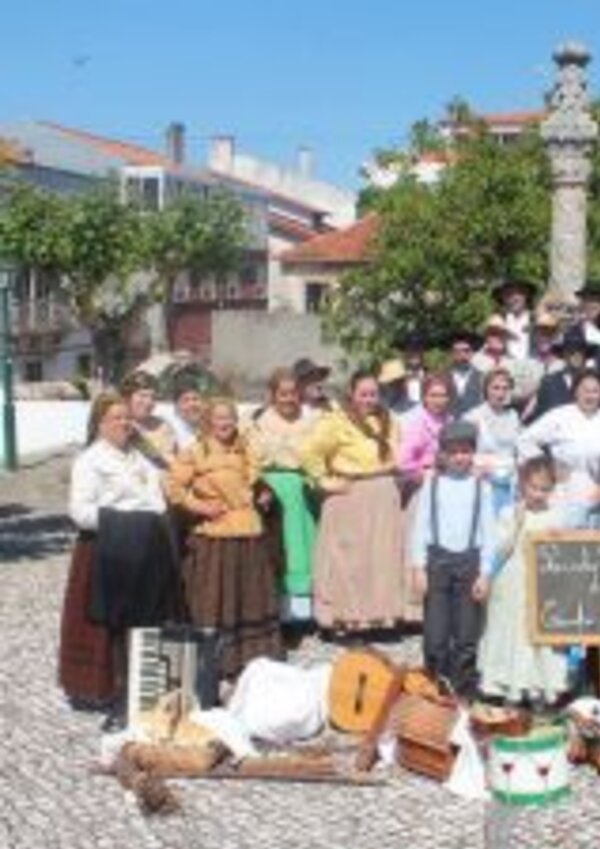 Grupo de pessoas em trajes tradicionais, com instrumentos e uma placa.