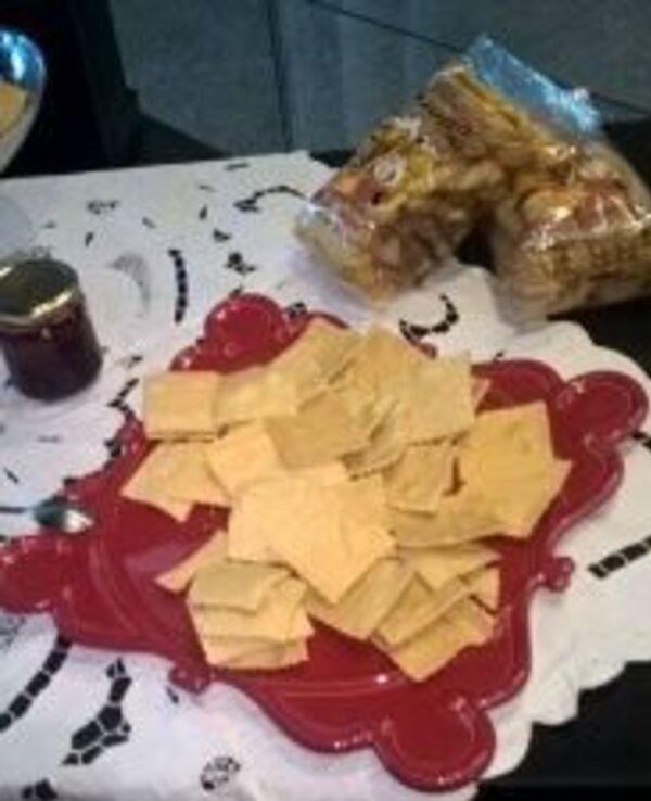 Prato vermelho com bolachas quadradas, ao fundo pacotes de biscoitos.