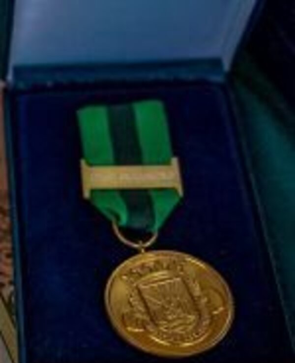 Medalha dourada com fita verde e preta, dentro de uma caixa azul.