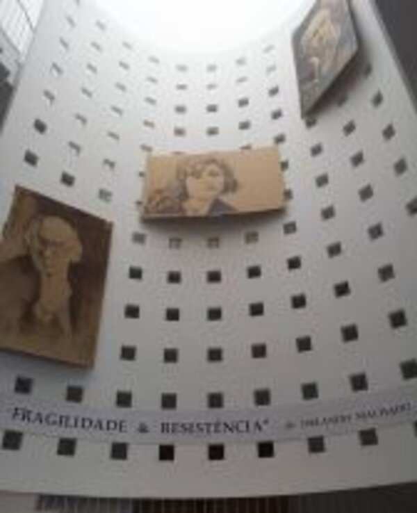 Interior de um espaço com pinturas em paredes brancas e uma faixa com texto.