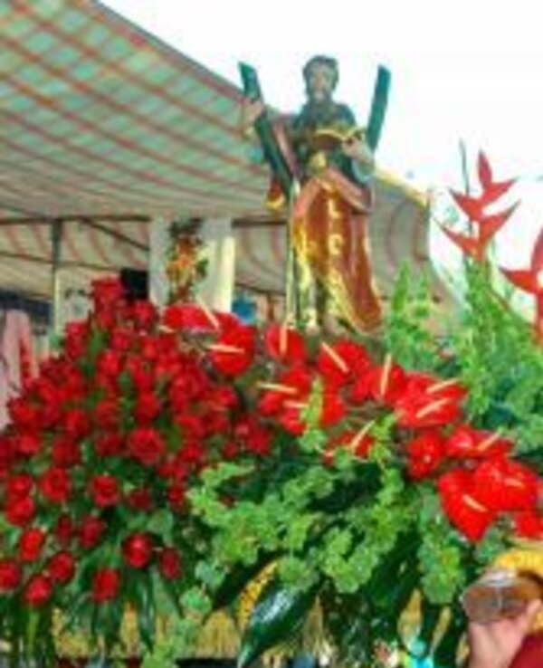 Estátua de um santo adornada com rosas vermelhas e folhagem verde.