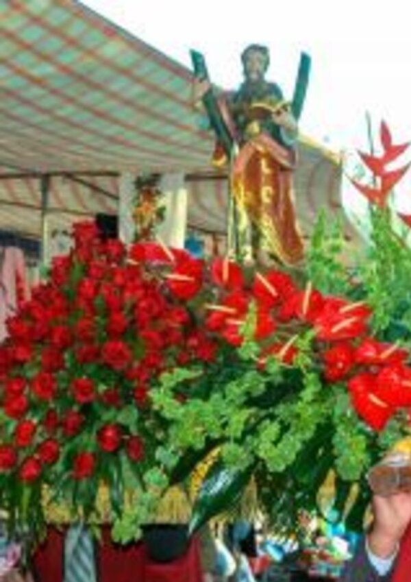 Estátua de um santo adornada com rosas vermelhas e folhagem verde.