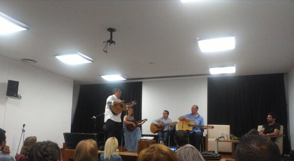 Um grupo de músicos a tocar instrumentos num palco, com público atento.