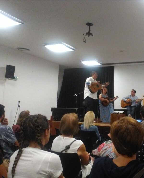 Um grupo de músicos a tocar instrumentos num palco, com público atento.