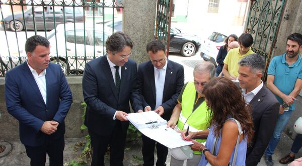Grupo de pessoas a discutir documentos numa rua, com carros ao fundo.