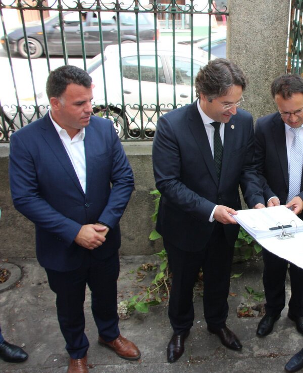 Grupo de pessoas a discutir documentos numa rua, com carros ao fundo.