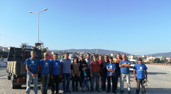 Grupo de pessoas sorridentes em um local ao ar livre, com céu azul ao fundo.