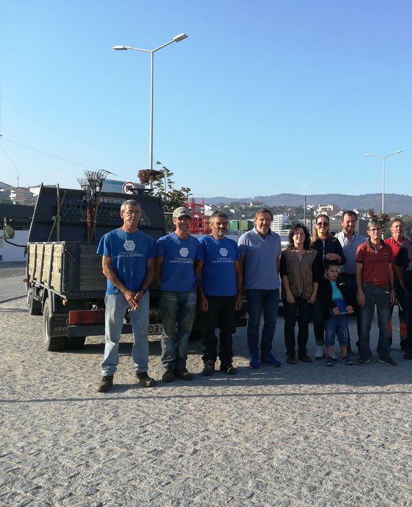Grupo de pessoas sorridentes em um local ao ar livre, com céu azul ao fundo.