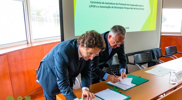 Dois homens em fato a assinar um protocolo de cooperação numa cerimónia.