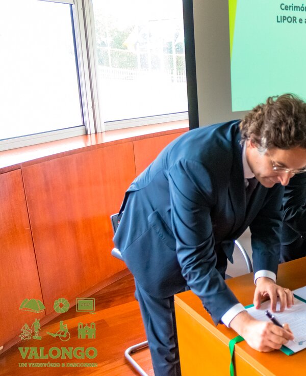 Dois homens em fato a assinar um protocolo de cooperação numa cerimónia.