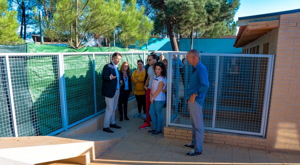 Grupo de pessoas a ouvir uma apresentação num espaço exterior com cercas.