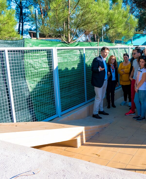 Grupo de pessoas a ouvir uma apresentação num espaço exterior com cercas.