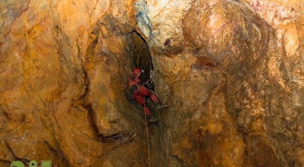 Um espeleólogo a descer uma fenda numa caverna com rochas coloridas.