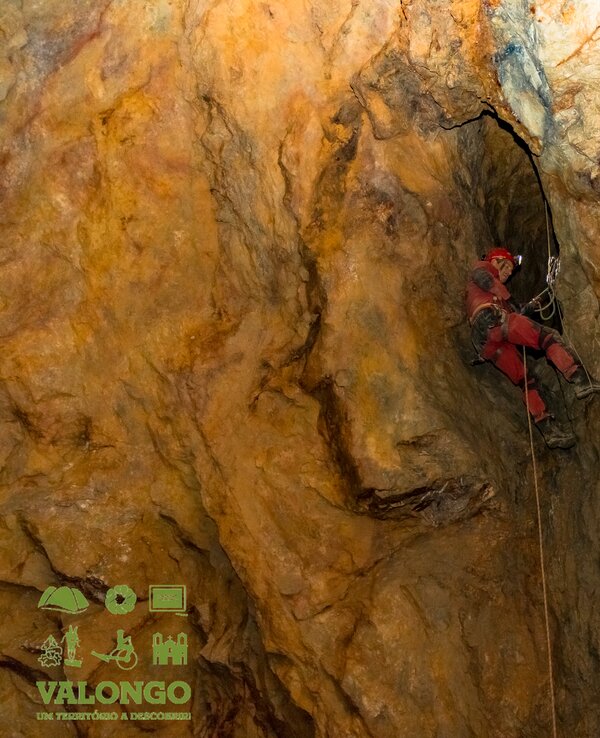 Um espeleólogo a descer uma fenda numa caverna com rochas coloridas.