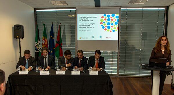 Mesa redonda com vários oradores e apresentação em fundo.