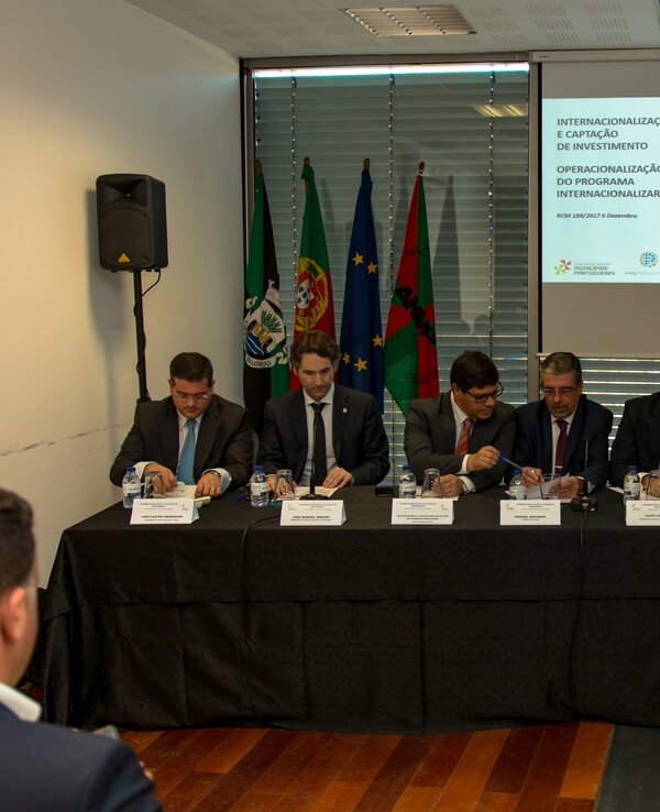 Mesa redonda com vários oradores e apresentação em fundo.