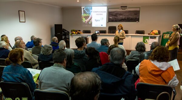 Público assistindo a uma palestra sobre compostagem em sala cheia.