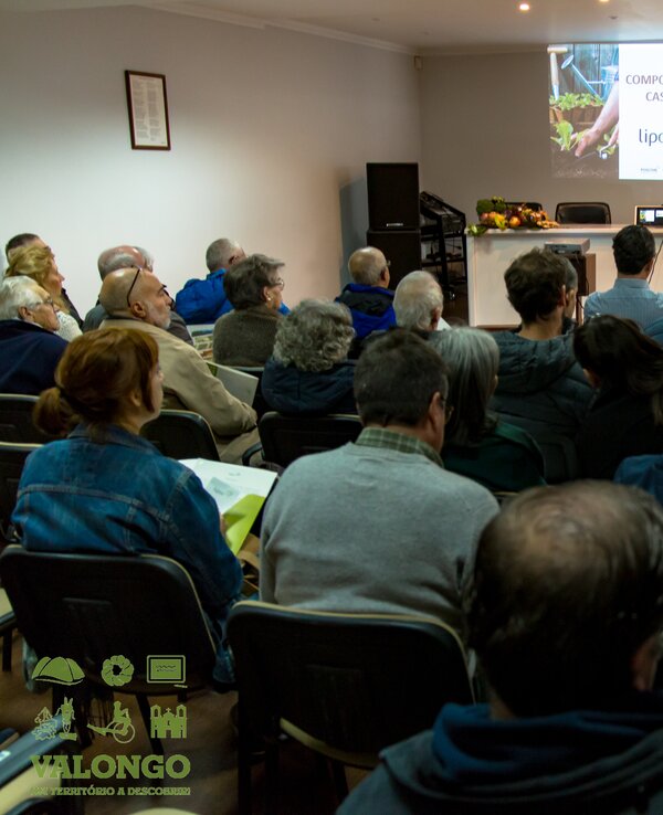 Público assistindo a uma palestra sobre compostagem em sala cheia.