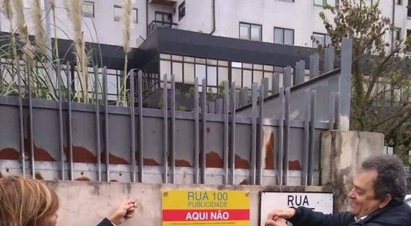 Duas pessoas a colocar um cartaz sobre publicidade numa parede.