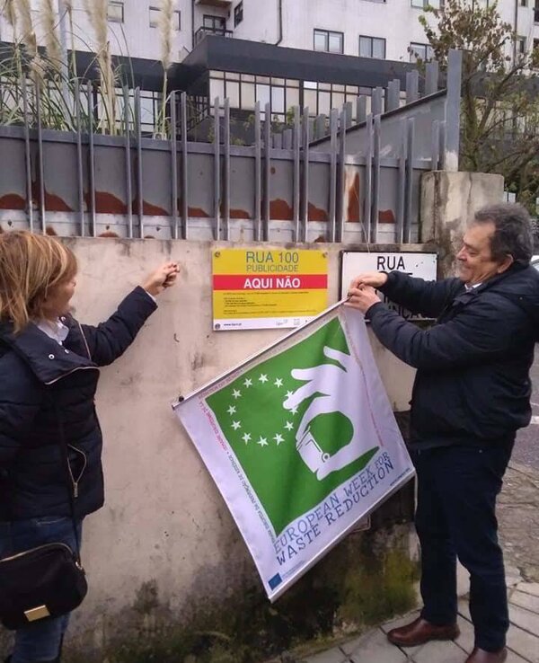 Duas pessoas a colocar um cartaz sobre publicidade numa parede.