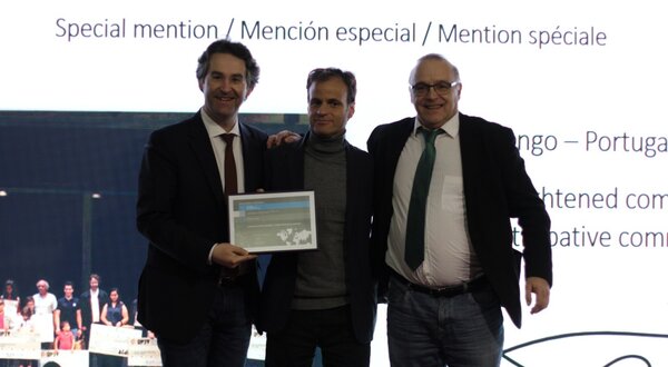 Três homens em palco, segurando um certificado de menção especial.