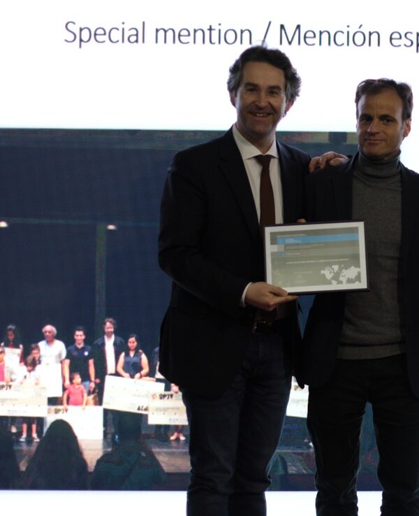 Três homens em palco, segurando um certificado de menção especial.