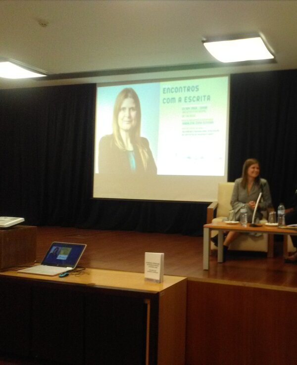 Duas pessoas sentadas em um painel, com apresentação ao fundo.