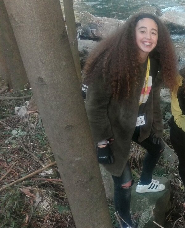 Grupo de jovens a explorar a natureza junto a um rio, com árvores ao redor.