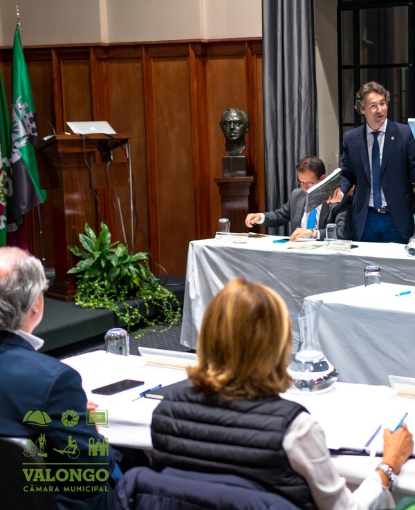 Reunião da câmara municipal com vários membros a discutir documentos.