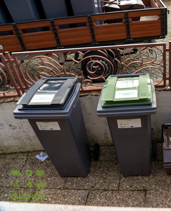 Quatro contentores de lixo coloridos para reciclagem, alinhados numa calçada.