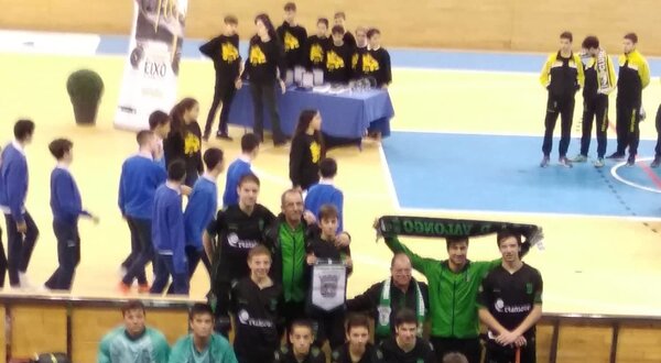 Equipa de hóquei em patins posando com bandeira e troféus em pavilhão desportivo.