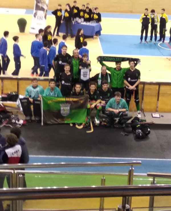 Equipa de hóquei em patins posando com bandeira e troféus em pavilhão desportivo.