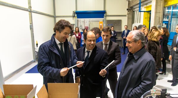 Grupo de homens em traje formal a discutir documentos numa fábrica.