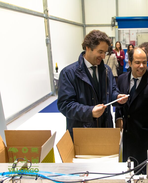 Grupo de homens em traje formal a discutir documentos numa fábrica.