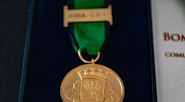 Medalha dourada com fita verde e preta, simbolizando uma distinção.