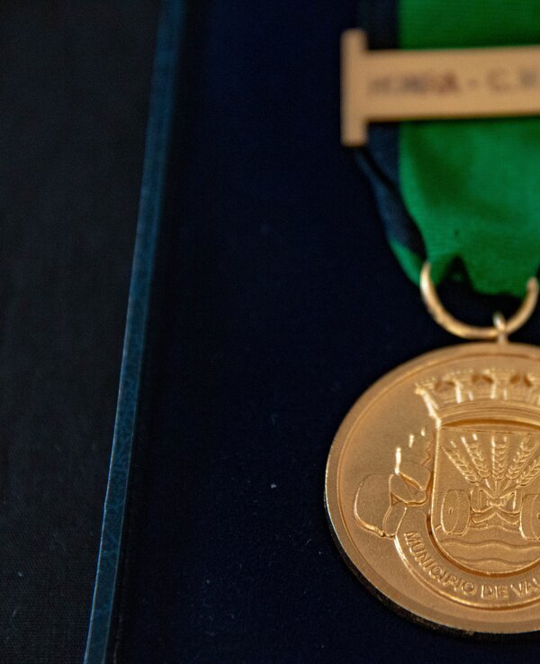 Medalha dourada com fita verde e preta, simbolizando uma distinção.