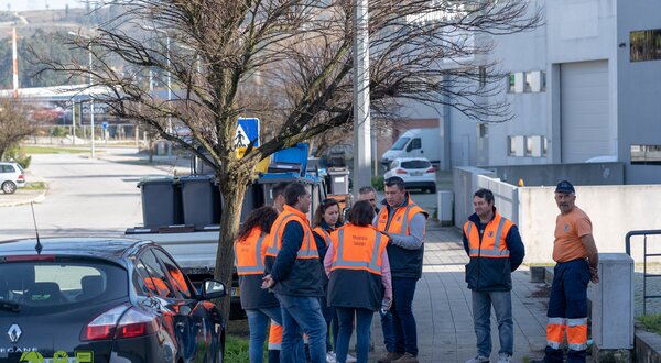 Grupo de pessoas em coletes laranja a discutir na rua, perto de carros.