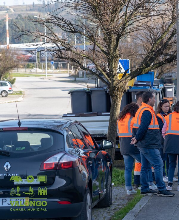 Grupo de pessoas em coletes laranja a discutir na rua, perto de carros.