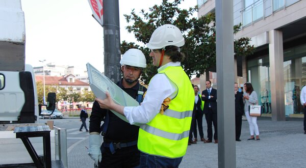 Dois trabalhadores com capacetes discutem um plano em frente a um edifício.