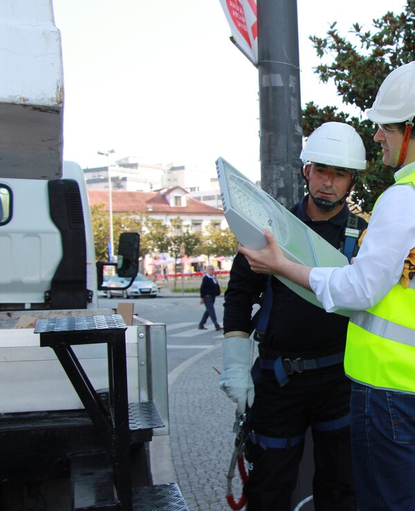 Dois trabalhadores com capacetes discutem um plano em frente a um edifício.