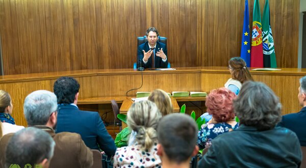 Reunião em câmara municipal com várias pessoas a ouvir um orador.