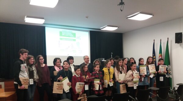 Grupo de crianças e adultos a receber prémios num evento, com diplomas nas mãos.