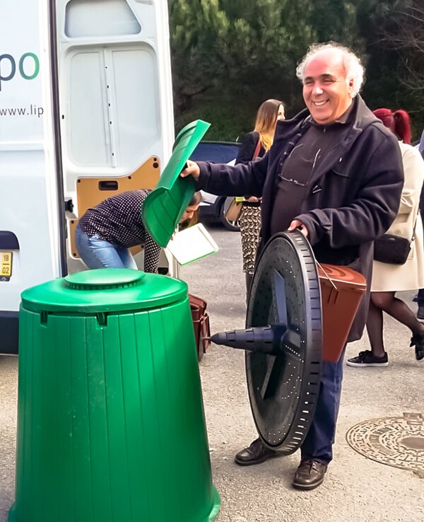 Um homem segura um compostor e um recipiente verde para resíduos orgânicos.